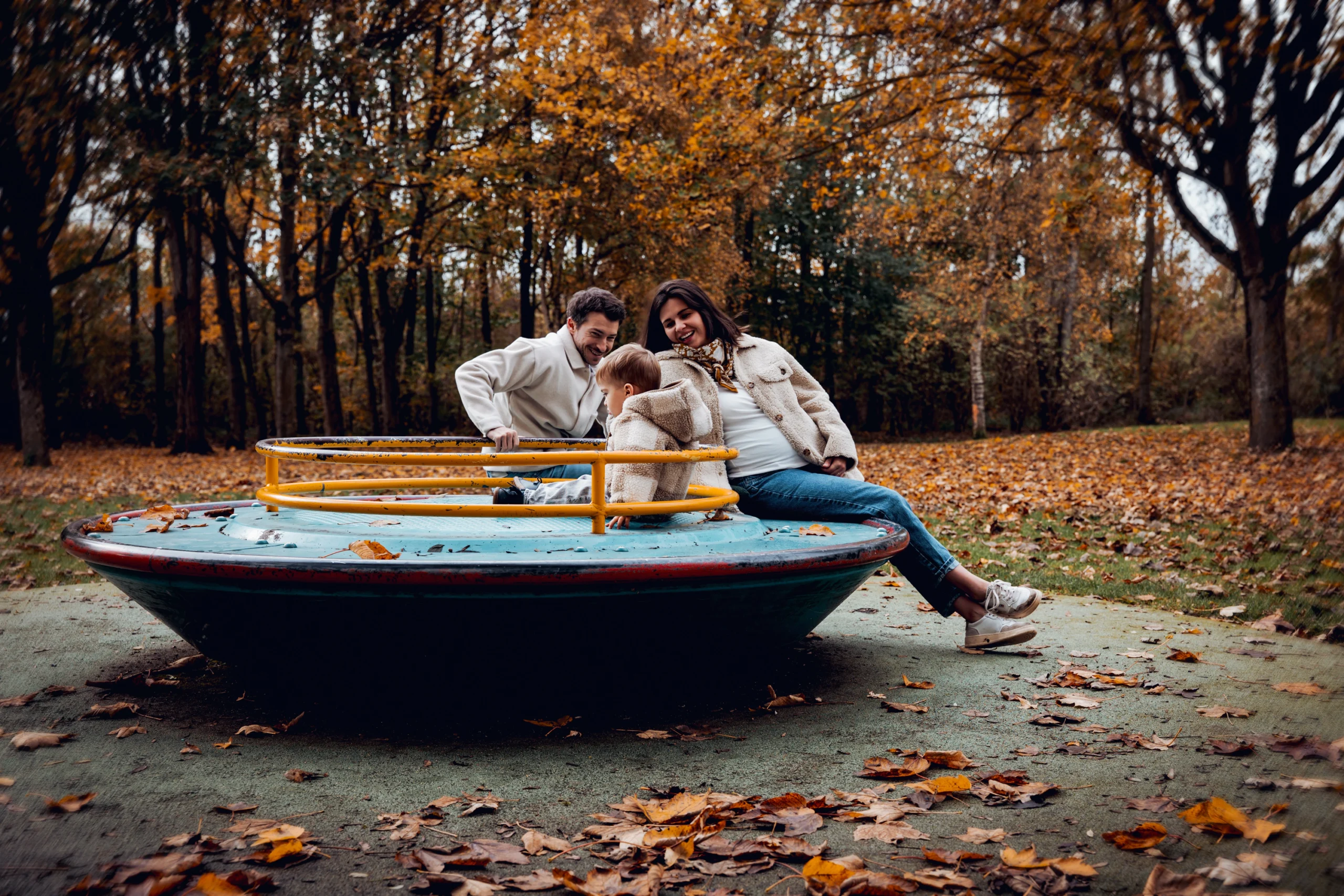 Séance photo grossesse en extérieur, famille complice sur un manège en forêt