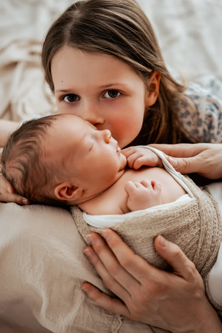 Portrait bébé en studio, nouveau-né blotti contre sa grande sœur dans les bras de son parent
