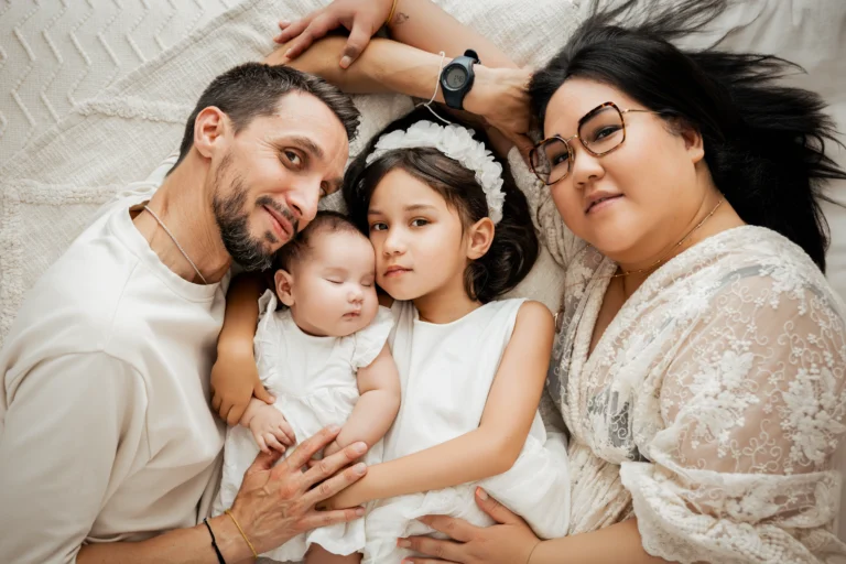 Séance photo bébé en studio, nouveau-né endormi dans les bras de ses parents entourée de sa grande sœur
